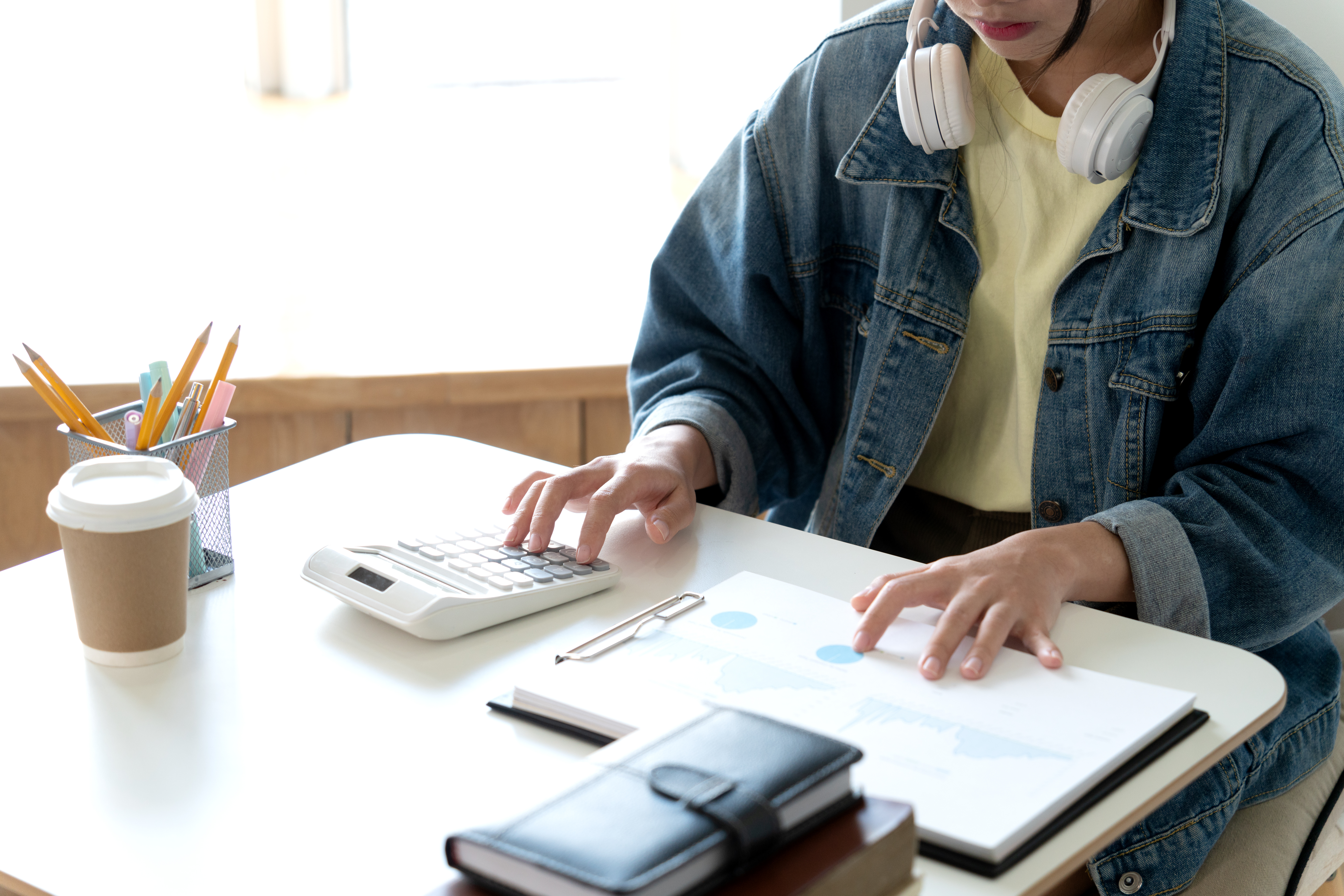 young teenage woman is using a calculator to calculate numbers from a graph chart in order to check work or homework for study in a private office or home.