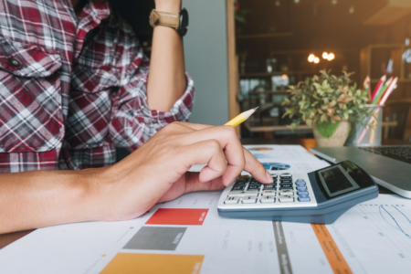 Close up of businessman or accountant hand holding pen working on laptop computer for calculate business data, accountancy document and calculator at office, business concept