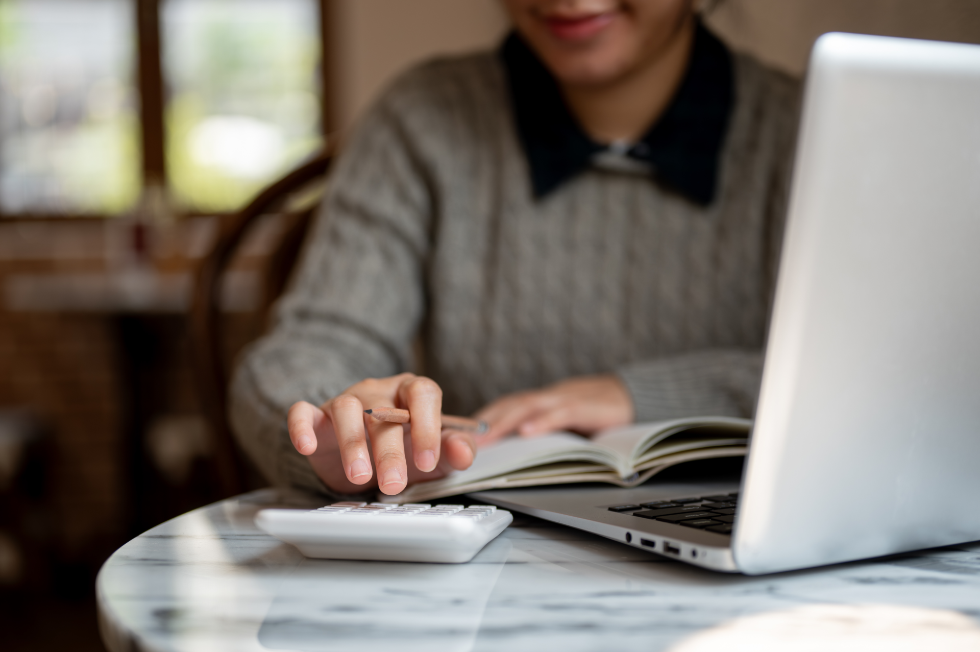 A cropped image of an Asian female college student is working remotely at a cafe, doing her homework, and using a calculator. studying, education, learning, financial