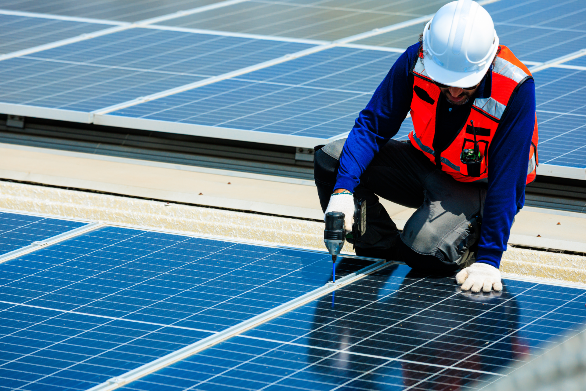 Solar technician using a power drill to install and maintain photovoltaic panels on a rooftop, representing renewable energy, skilled engineering, clean electricity and workplace safety.