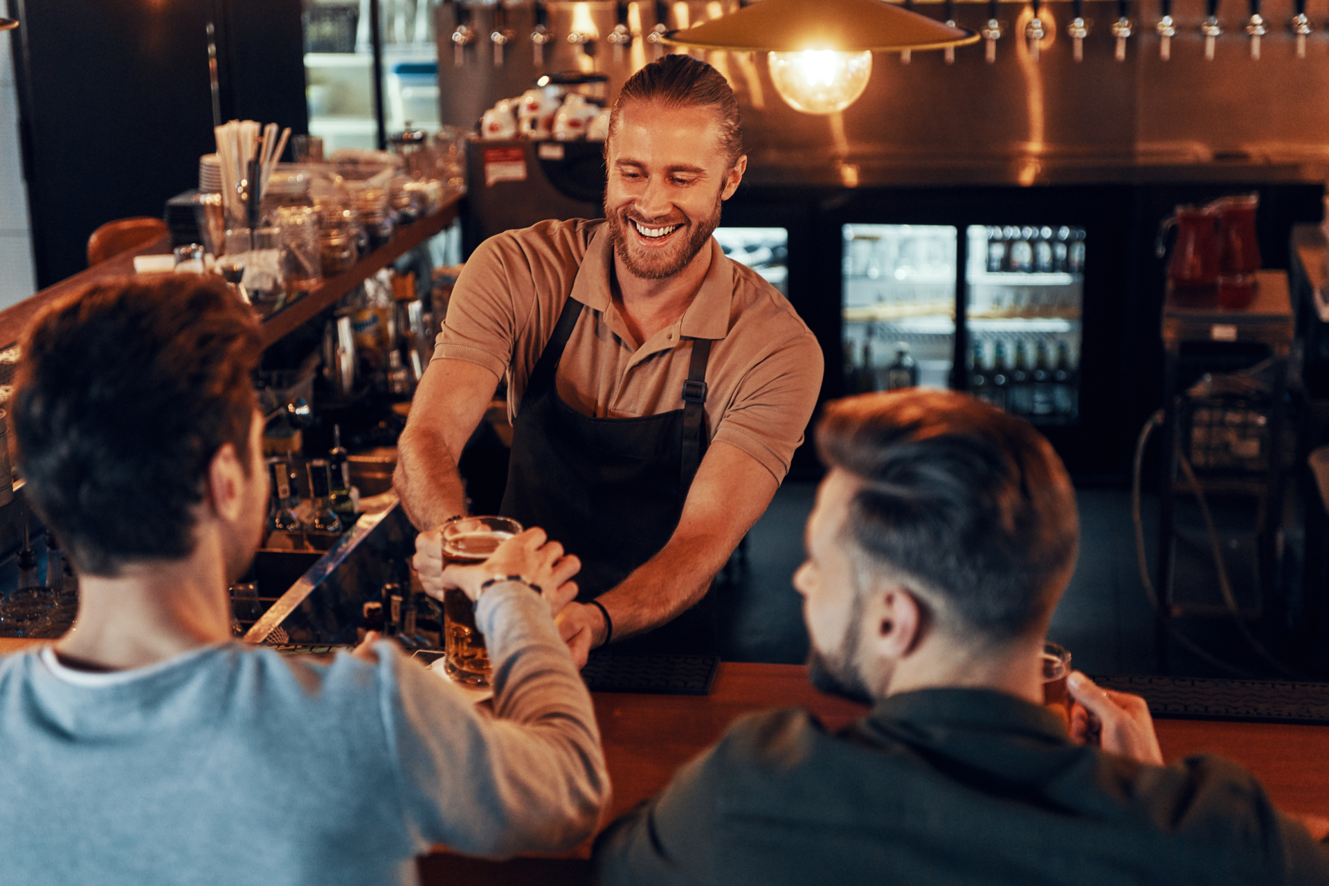 Top view of bartender serving beer to young men while standing at the bar counter in pub.